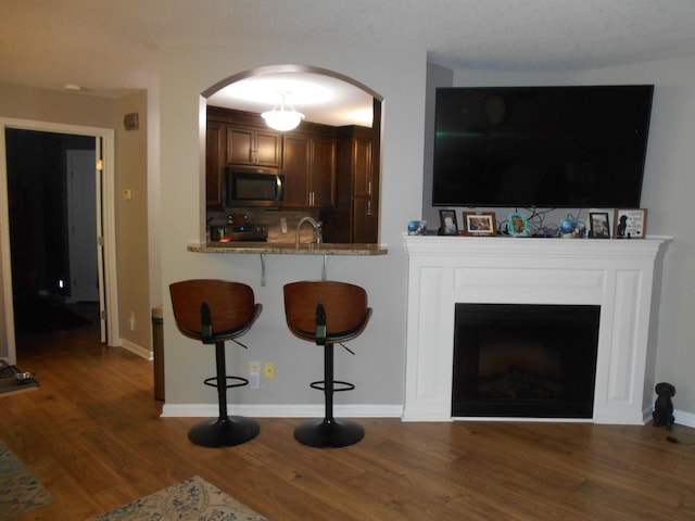 living room featuring arched walkways, dark wood-style flooring, a fireplace, and baseboards