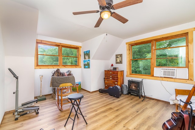 sitting room with a wood stove, cooling unit, wood finished floors, healthy amount of natural light, and lofted ceiling