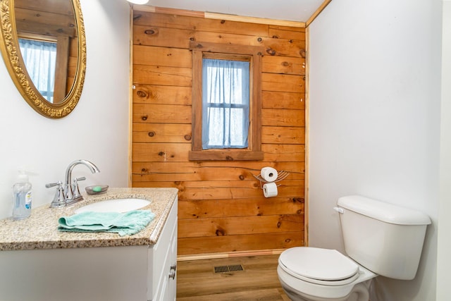 bathroom featuring toilet, vanity, wood finished floors, and wooden walls