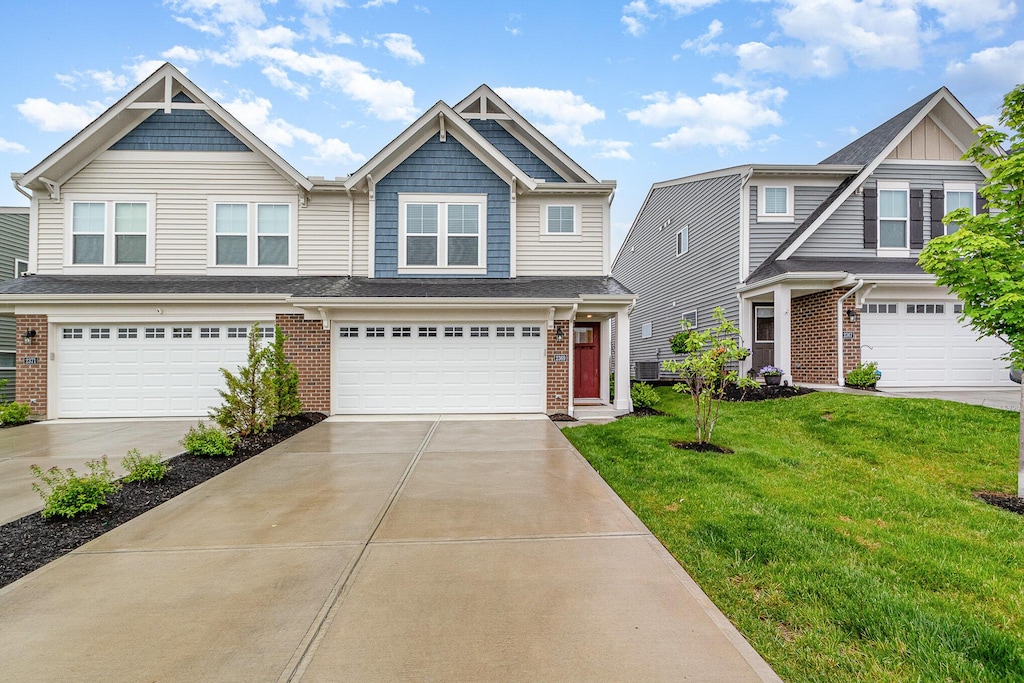 craftsman-style home featuring a front yard, an attached garage, brick siding, and driveway