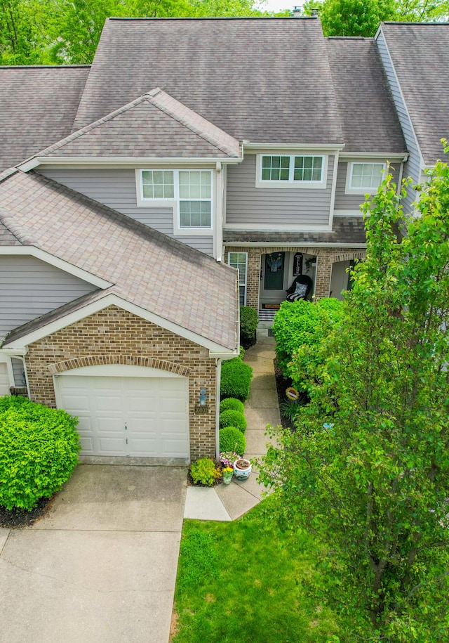 multi unit property featuring concrete driveway, brick siding, a garage, and a shingled roof