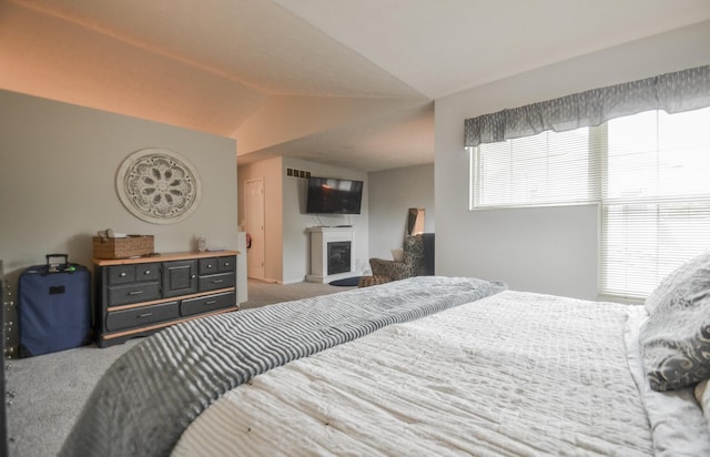 carpeted bedroom featuring vaulted ceiling, a glass covered fireplace, and multiple windows