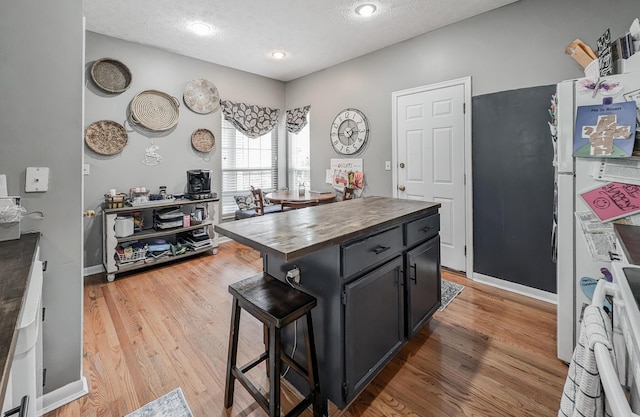 kitchen featuring butcher block counters, a textured ceiling, light wood finished floors, a breakfast bar, and dark cabinetry