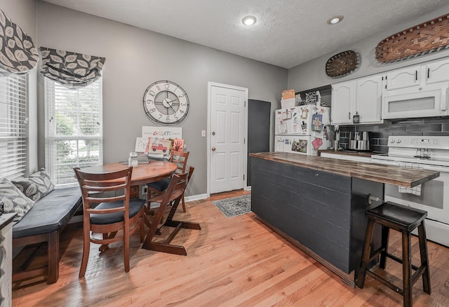 kitchen featuring white appliances, butcher block counters, white cabinets, light wood finished floors, and decorative backsplash