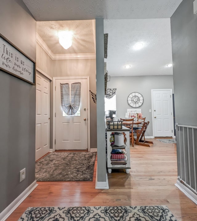 entryway with wood finished floors, baseboards, a textured ceiling, crown molding, and recessed lighting