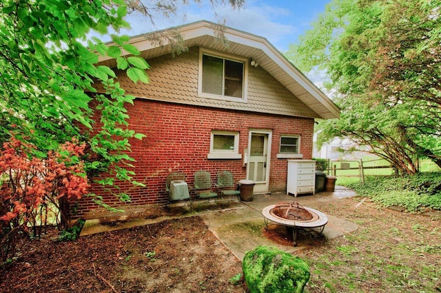 rear view of house featuring brick siding, an outdoor fire pit, and fence