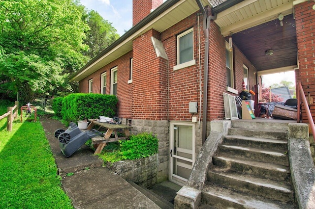 view of side of home featuring brick siding, a chimney, and a porch
