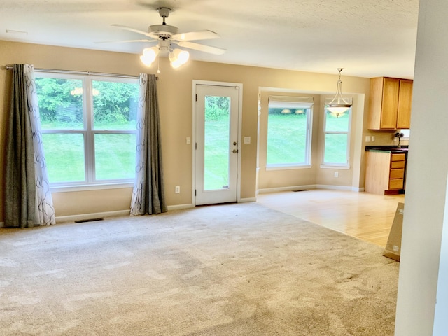 unfurnished living room with light carpet, a ceiling fan, and baseboards