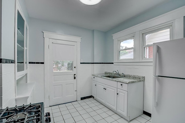 kitchen featuring freestanding refrigerator, a sink, white cabinetry, light tile patterned flooring, and tile walls