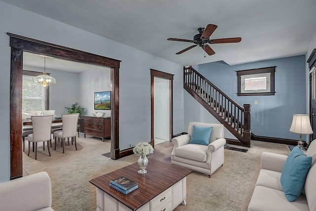 living room with light carpet, stairs, a chandelier, baseboards, and a ceiling fan