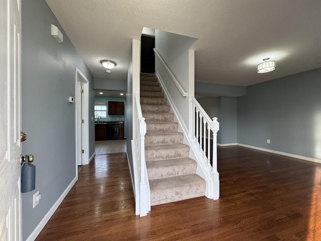 stairs featuring wood finished floors, baseboards, and a textured ceiling