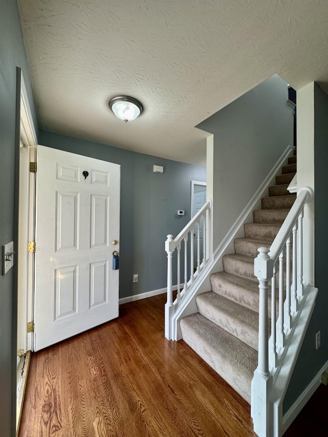foyer with stairs, wood finished floors, baseboards, and a textured ceiling