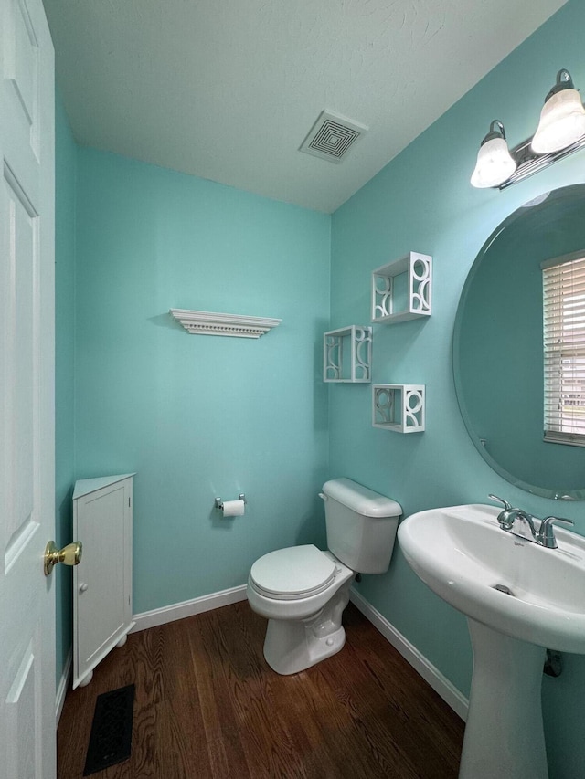 half bathroom with wood finished floors, baseboards, toilet, and a sink