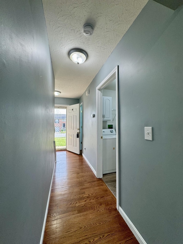 hallway with washer / clothes dryer, wood finished floors, baseboards, and a textured ceiling