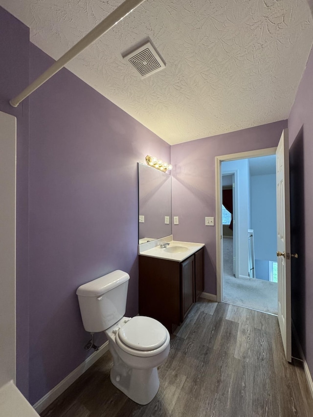 bathroom featuring wood finished floors, toilet, a textured ceiling, vanity, and baseboards