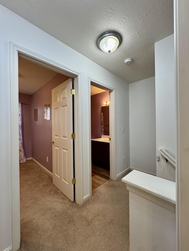 hallway featuring light colored carpet and baseboards
