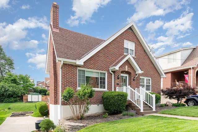 tudor home featuring brick siding, a shed, a chimney, and a front yard