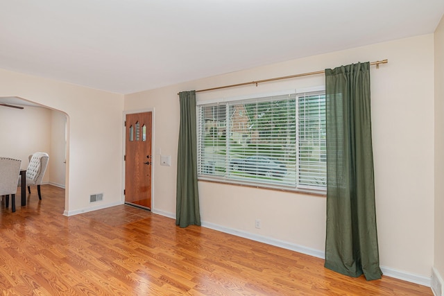 empty room featuring light wood-type flooring, arched walkways, and baseboards