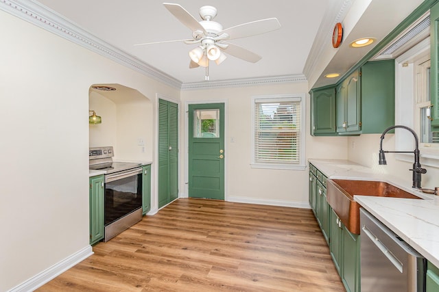 kitchen featuring green cabinetry, stainless steel appliances, a sink, light wood-style flooring, and baseboards