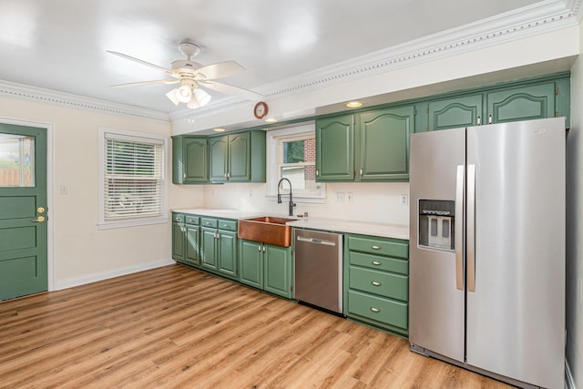 kitchen with stainless steel appliances, a sink, green cabinetry, and ornamental molding