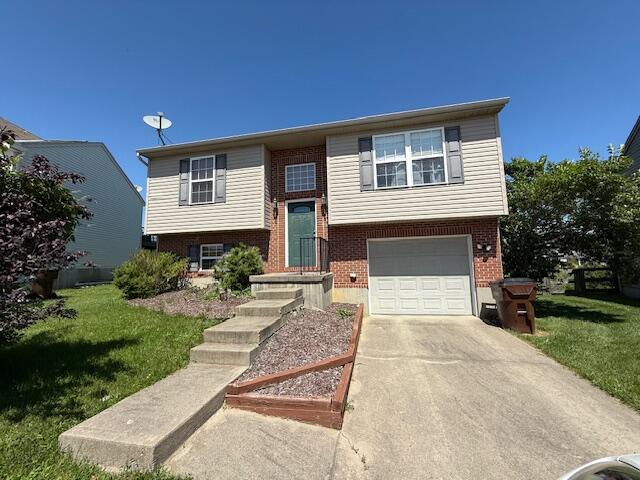 raised ranch featuring an attached garage, brick siding, a front lawn, and driveway