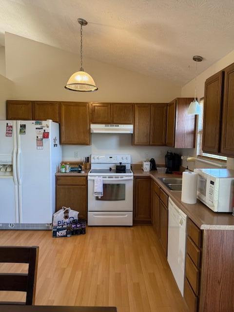 kitchen with white appliances, under cabinet range hood, vaulted ceiling, decorative light fixtures, and light wood-style flooring