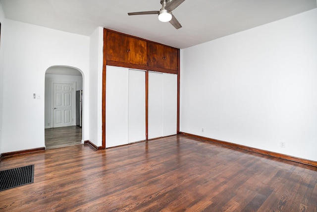 unfurnished bedroom with arched walkways, wood finished floors, a closet, baseboards, and a ceiling fan