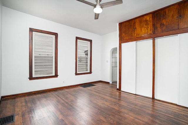 unfurnished bedroom with arched walkways, dark wood-type flooring, baseboards, a closet, and ceiling fan