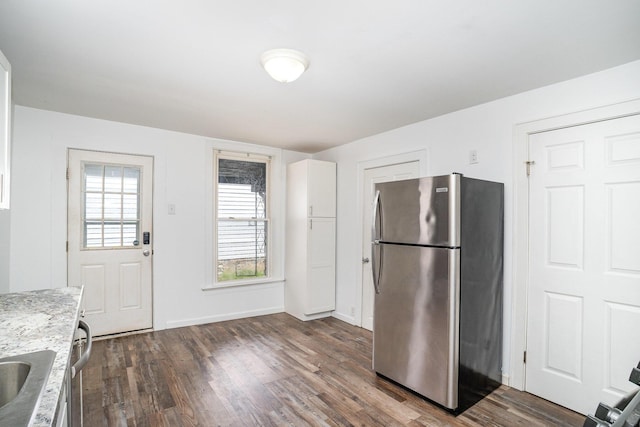kitchen with freestanding refrigerator, dark wood-style flooring, light stone countertops, baseboards, and white cabinets