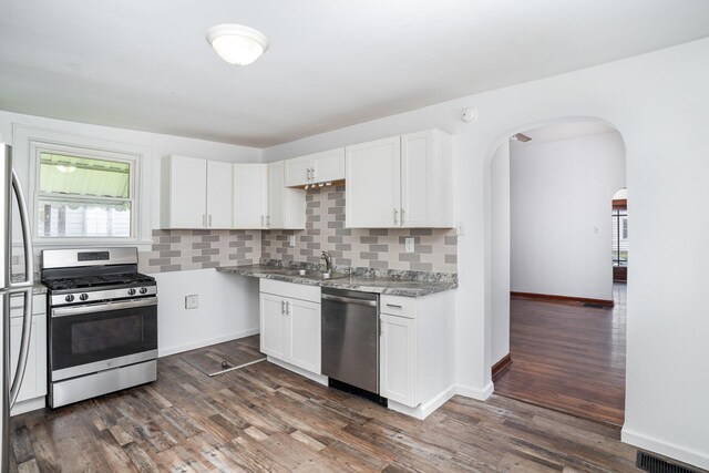 kitchen with stainless steel appliances, arched walkways, decorative backsplash, and dark wood-type flooring