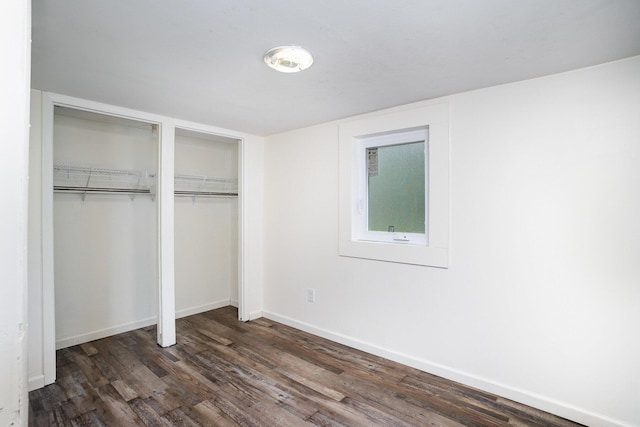 unfurnished bedroom featuring dark wood-type flooring, baseboards, and multiple closets