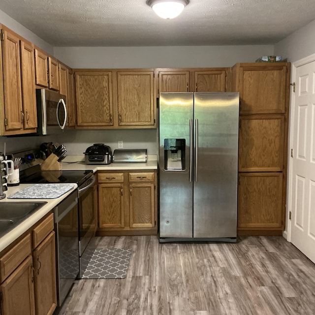 351 Deepwoods Dr, Newport, KY 41076 - kitchen featuring stainless steel appliances, light countertops, light wood finished floors, brown cabinets, and a textured ceiling