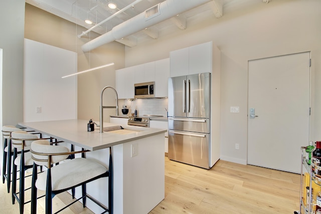 120 Main St Unit 205, Newport, KY 41071 - kitchen featuring appliances with stainless steel finishes, light wood-style floors, a breakfast bar, tasteful backsplash, and white cabinetry