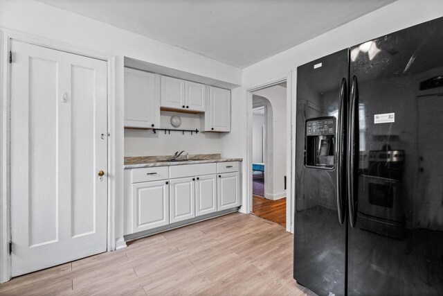 309 Hawthorne St, Covington, KY 41014 - kitchen with black refrigerator with ice dispenser, arched walkways, light wood-style floors, light countertops, and white cabinetry