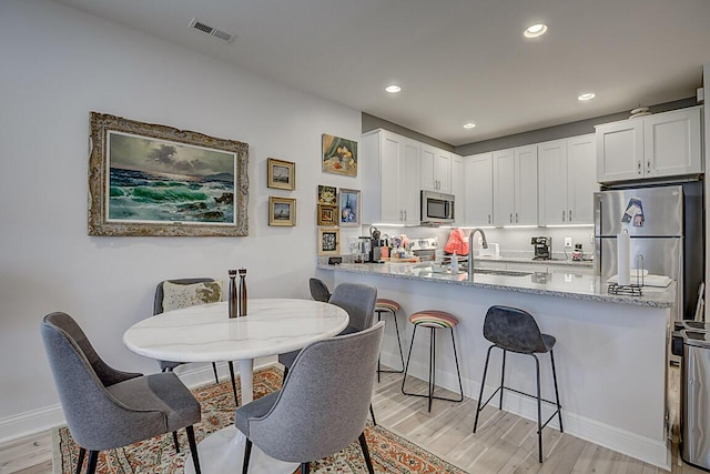 805 Ann St, Newport, KY 41071 - kitchen with appliances with stainless steel finishes, light wood-style flooring, a kitchen breakfast bar, white cabinets, and a peninsula
