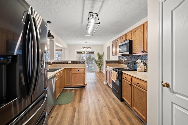 10335 Mackay Ct, Independence, KY 41051 - kitchen featuring stainless steel appliances, light wood finished floors, a peninsula, backsplash, and hanging light fixtures