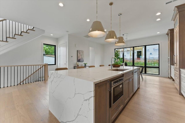 76 W 13th St Unit 34, Newport, KY 41071 - kitchen featuring light wood-style flooring, recessed lighting, a kitchen island with sink, decorative light fixtures, and light stone countertops