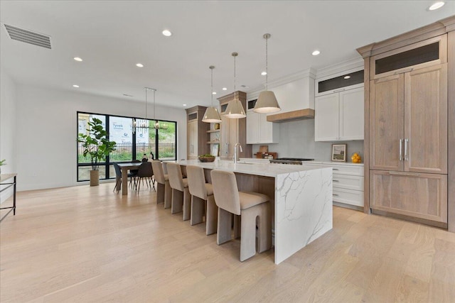 76 W 13th St Unit 34, Newport, KY 41071 - kitchen featuring light wood-style floors, an island with sink, recessed lighting, hanging light fixtures, and glass insert cabinets
