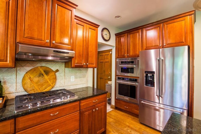 2507 Woodstone Way, Villa Hills, KY 41017 - kitchen with appliances with stainless steel finishes, under cabinet range hood, dark stone countertops, light wood finished floors, and decorative backsplash