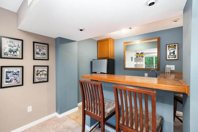 10234 Hempsteade Dr, Union, KY 41091 - kitchen featuring freestanding refrigerator, a kitchen breakfast bar, light countertops, brown cabinets, and light colored carpet