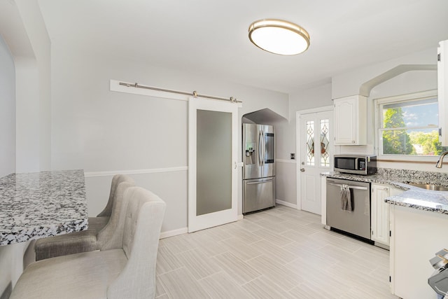 65 W Crittenden Ave, Fort Wright, KY 41011 - kitchen featuring appliances with stainless steel finishes, light stone countertops, white cabinets, arched walkways, and a barn door