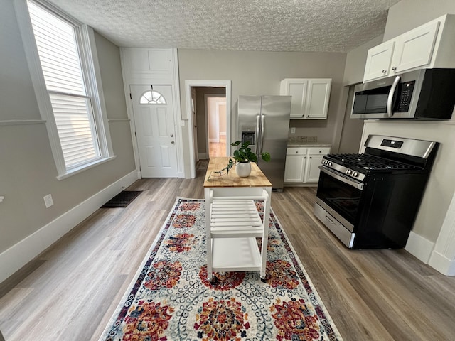 626 W 12th St, Covington, KY 41011 - kitchen with appliances with stainless steel finishes, light wood finished floors, white cabinets, and a textured ceiling