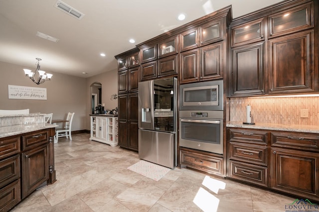 kitchen featuring dark brown cabinetry, hanging light fixtures, light stone counters, decorative backsplash, and appliances with stainless steel finishes