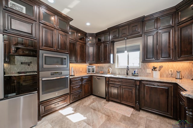 kitchen with light stone countertops, appliances with stainless steel finishes, dark brown cabinetry, and sink