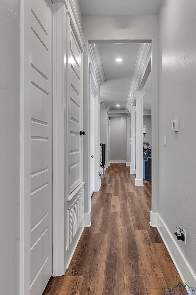 hallway featuring dark wood-type flooring, decorative columns, baseboards, and ornamental molding