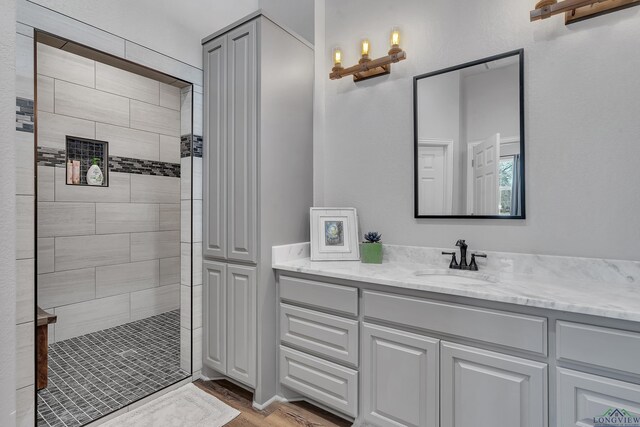 full bathroom with tiled shower, vanity, and wood finished floors