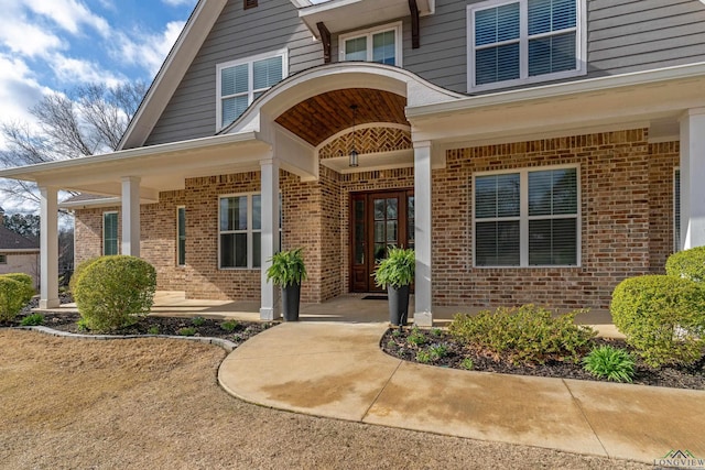 doorway to property with a porch and brick siding