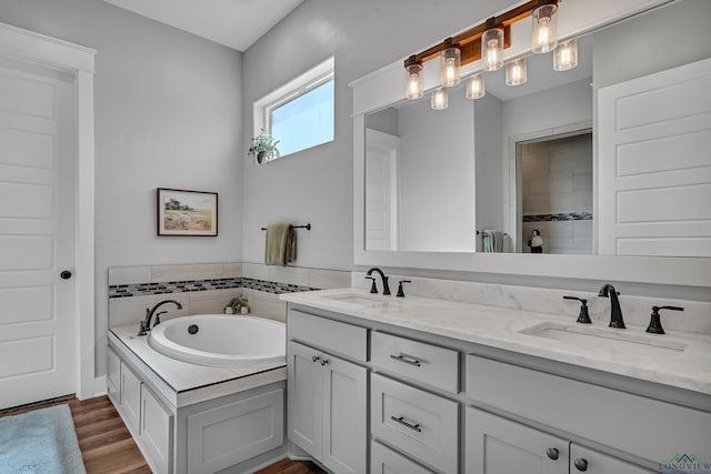 bathroom with double vanity, wood finished floors, a garden tub, and a sink