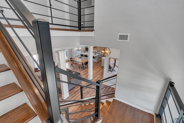 stairway with visible vents, baseboards, a chandelier, a high ceiling, and wood finished floors