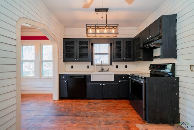 kitchen featuring dark hardwood / wood-style flooring, wooden walls, sink, black appliances, and pendant lighting